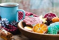 A cup of hot tea stands on a wooden table next to a wooden plate on which are gingerbread cookies made from orange slices against Royalty Free Stock Photo