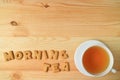 Cup of hot tea beside with the word MORNING TEA spelling with cookies biscuits on wooden table Royalty Free Stock Photo
