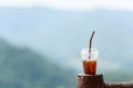 Cup ice coffee on wood tree outdoor over mountains landscape with sunlight. Royalty Free Stock Photo