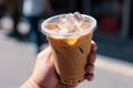 Cup of iced latte cappuccino coffee in hand on city street. Takeaway coffee drink Generative AI. Royalty Free Stock Photo