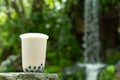 a cup of iced milktea with tapiocas and guiling jelly in front of waterfall