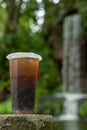 a cup of iced tea with brown sugar in front of waterfall at vertical composition Royalty Free Stock Photo