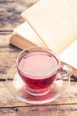 Cup of karkade tea with old opened book on old weathered table Royalty Free Stock Photo