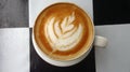 a cup of latte coffee with flower-shaped latte art with a white cup and in a black and white square background