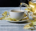 Cup of linden tea with liquid and flowing teapot or blooming tilia, basswood, on rustic vintage white wooden table. Herbal tea con Royalty Free Stock Photo