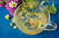 A cup of linden tea and medicinal herbs on a old blue wooden table. fresh clover, chamomile and linden. herbal tea. flu and cold r