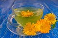 A cup of marigold tea and marigold flowers on a blue wooden background. Royalty Free Stock Photo