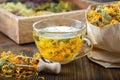 Cup of marigold tea and paper bag of dry calendula flowers. Medicinal herbs in wooden crate on background. Royalty Free Stock Photo