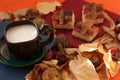 A cup of milk coffee, several pieces of homemade pie with jam, chestnuts and dry autumn leaves on a red surface