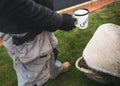 A cup of milky coffee being held by a workman in overalls by a wheelbarrow standing on grass in a garden or back yard. Royalty Free Stock Photo