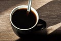 A cup of morning black coffee without milk with a spoon in a black cup on a wooden table. Shadows from the morning sun Royalty Free Stock Photo