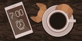 A cup of morning coffee with croissants and a mobile phone on a wooden table.