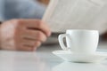 Cup of morning coffee on worktable with businessman reading news