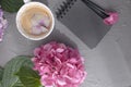 A cup of morning fragrant coffee and pink hydrangea flowers, on a gray background, free space for text and a black notepad. Card,
