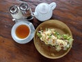 Cup of morning tea with teapot, white and brown sugar. With scrambled eggs and vegetable on brown bread for breakfast on a plate.