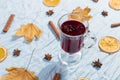A cup of mulled wine with spices, dry leaves and oranges on the table. Autumn mood, a method to keep warm in the cold, copy space