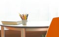 A cup with pencils and a corner of the book on the table by the window. Blurred background. Workplace for study. lightful room