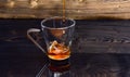 Cup pouring with water or tea with splashes on dark wooden background. Brewing tea concept. Glass with tea pouring with Royalty Free Stock Photo