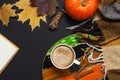 Cup of pumpkin cocoa or coffee, opened notebook, pumpkin, cinnamon, yellow autumn maple leaf, checkered plaid on black background