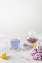 Cup of purple tea with lemon, teapot, bouquet of blooming lilac on light background. Spring tea drinking. Greeting card,