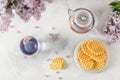 Cup of purple tea with lemon, teapot, waffles and a bouquet of blooming lilac on light background. Spring tea drinking. Greeting