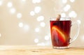 A cup with red mulled wine stands on a wooden tray on a light color background with bokeh