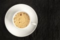 A cup of regular coffee with foam on a dark black background