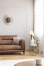 Cup on round wooden table in grey living room interior with blurred brown couch