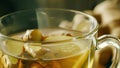 A cup of steaming ginger tea with floating slices of ginger root and a squeeze of lemon. Ginger is a wellknown herb for