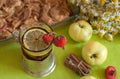 A cup of strong black tea with a lemon slice, an apple pie, a bouquet of chamomiles, cinnamon sticks, ripe apples and mature hips Royalty Free Stock Photo