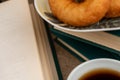 A cup of strong tea on a saucer, donuts on a plate and a stack of books on the table