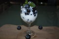 Cup sweated by cold natural white yogurt mixed with jumo blueberries and fresh mint leaf ornament placed on wooden board with trio Royalty Free Stock Photo