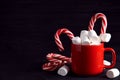 Cup of tasty cocoa with marshmallows and Christmas candy canes on black wooden table. Space for text