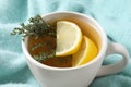 Cup of tasty herbal tea with thyme and lemon on turquoise fabric, closeup