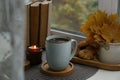 Cup of tasty hot drink near books, burning candle and cookies on windowsill. Autumn coziness
