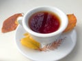 Cup of tea with autumn leaves, reflection of sky and trees inside the cup, on white table. Royalty Free Stock Photo