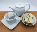 Cup with tea bags, teapot and chocolate wafers on wooden table, white background Royalty Free Stock Photo