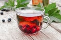 A cup of tea with black currants on a wooden table next to green leaves and currant berries Royalty Free Stock Photo