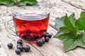 A cup of tea with black currants on a wooden table next to green leaves and currant berries Royalty Free Stock Photo