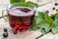 A cup of tea with black currants on a wooden table next to green leaves and currant berries Royalty Free Stock Photo