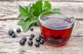 A cup of tea with black currants on a wooden table next to green leaves and currant berries Royalty Free Stock Photo