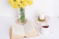 A cup tea, book, candle and daffodils in glass vase. Cozy home, reading or studying concept Royalty Free Stock Photo