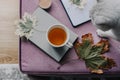 cup of tea with a book in the interior with autumn leaf, notebook and cat, hygge concept