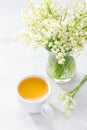 Cup of tea and bouquet of Lilies of the Valley in glass vase on rustic table