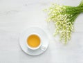 Cup of tea and bouquet of Lilies of the Valley on white rustic table