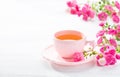 Cup of tea and branch of small pink roses on white rustic table