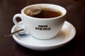 Cup of tea with Caffe Nero logo on white teacup with saucer and spoon on dark background.