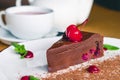 A cup of tea with a chocolate brownie cake with cherries and mint