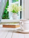 A cup of tea or coffee and a book on a white wooden antique retro table and a bouquet of lily-of-the-valley flowers on a window si Royalty Free Stock Photo