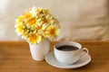 A cup of tea/coffee and a bouquet of daisies in a vase on a wooden tray on a light soft background